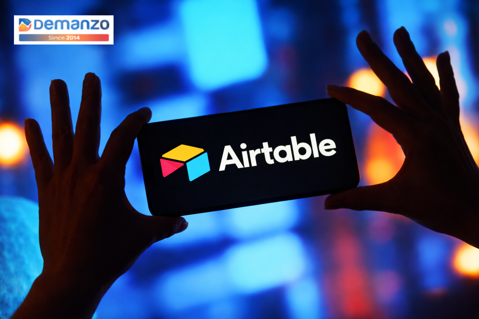 Silhouetted hands holding a phone displaying the Airtable logo, with a colorful blurred background